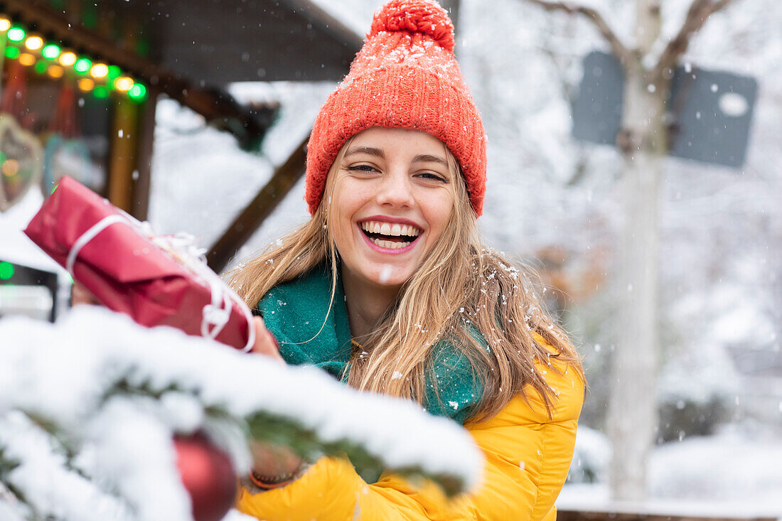 Lächelnde junge Frau mit Weihnachtsgeschenk in der Hand im Freien