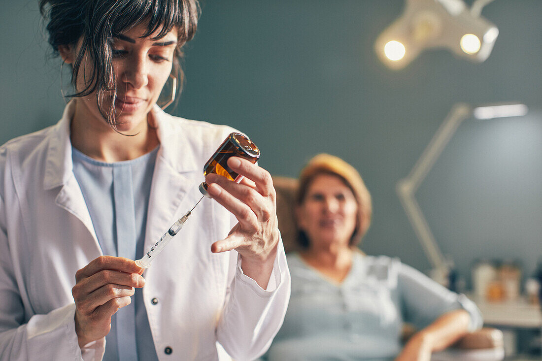 Female doctor preparing botox injection, patient in background
