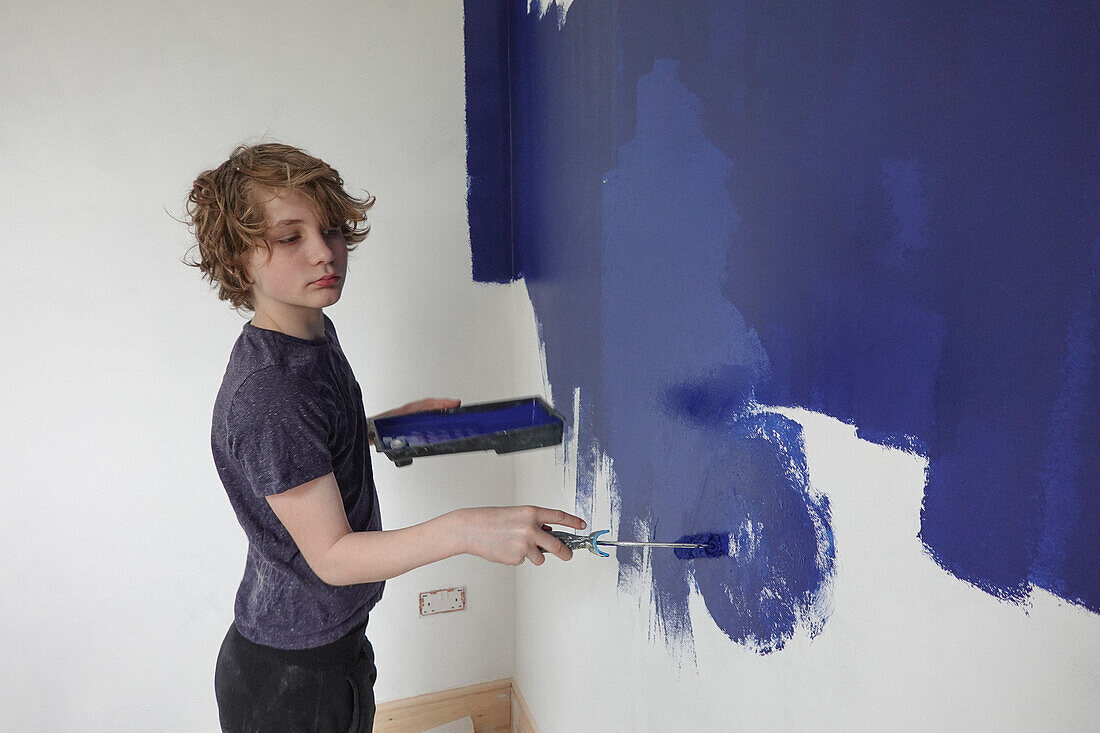 Boy painting wall with blue paint