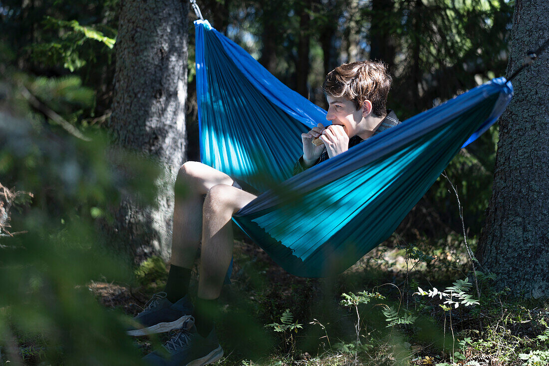 Junge (16-17) entspannt sich in einer Hängematte im Wald