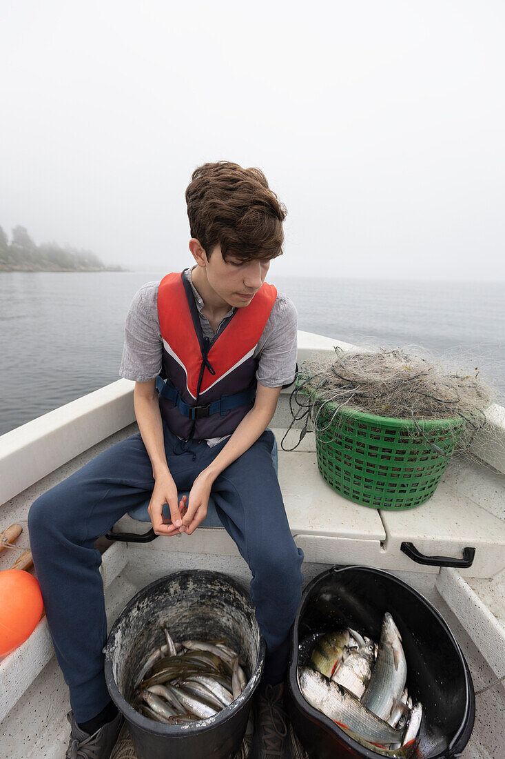 Boy (15-16) sitting in boat on foggy lake