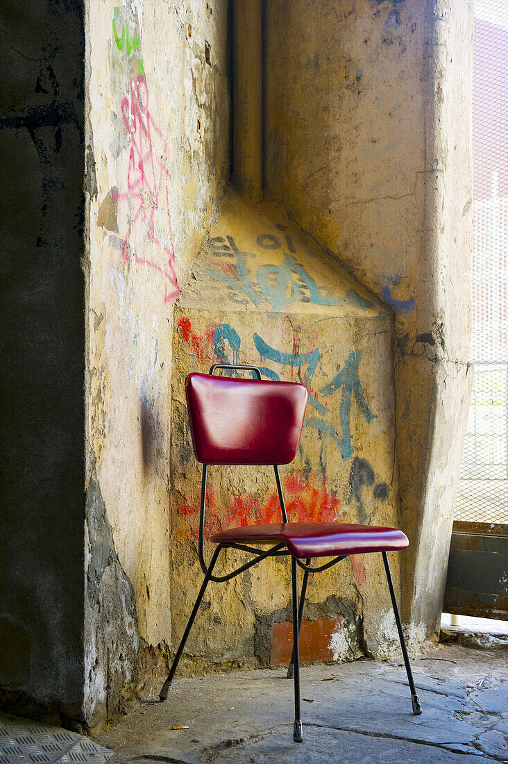 Ein roter Stuhl sitzt neben einer verwitterten Wand mit gemalten Graffiti; Barcelona, Spanien