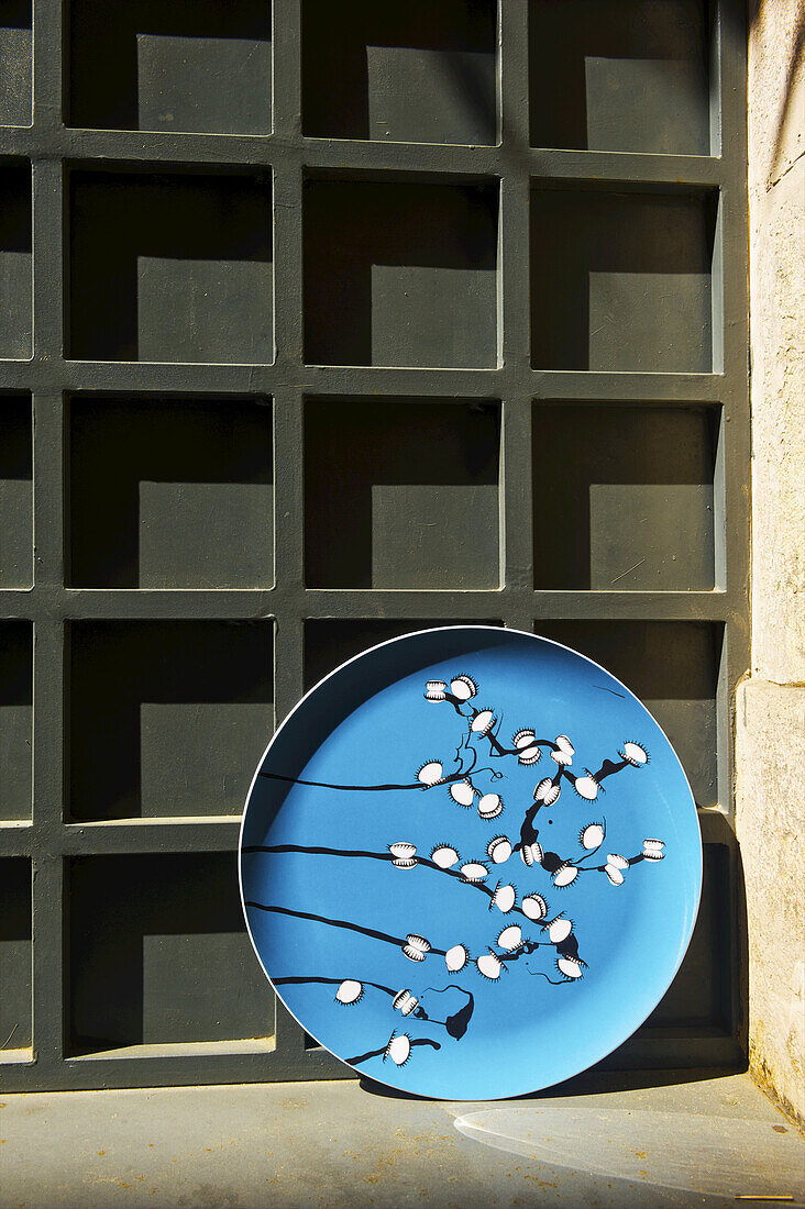 Ein blauer dekorativer Teller lehnt an einer Wand mit einer quadratischen Blockfassade; Barcelona, Spanien.