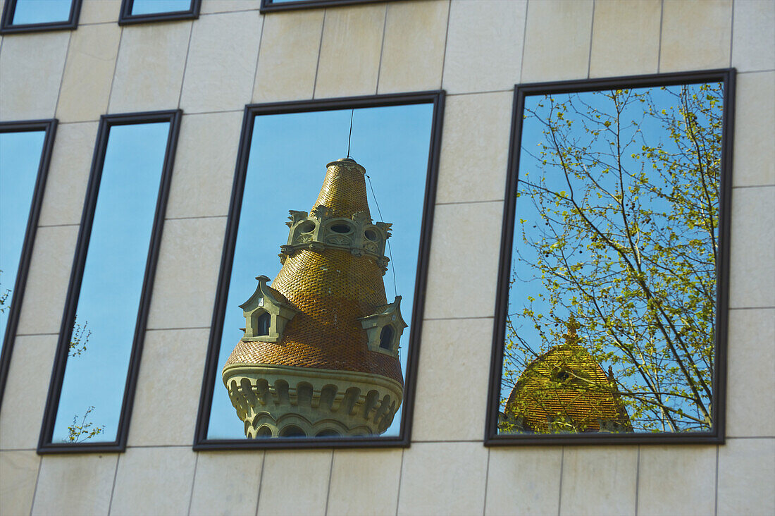 Spiegelung eines einzigartigen Turms, eines Baums und des blauen Himmels in einem Gebäudefenster; Barcelona, Spanien