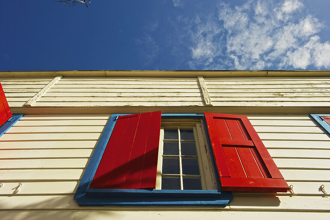 Low Angle View Of A Yellow Building With Bright Red Shutters Over A Window; Carlisle Bay, Antigua