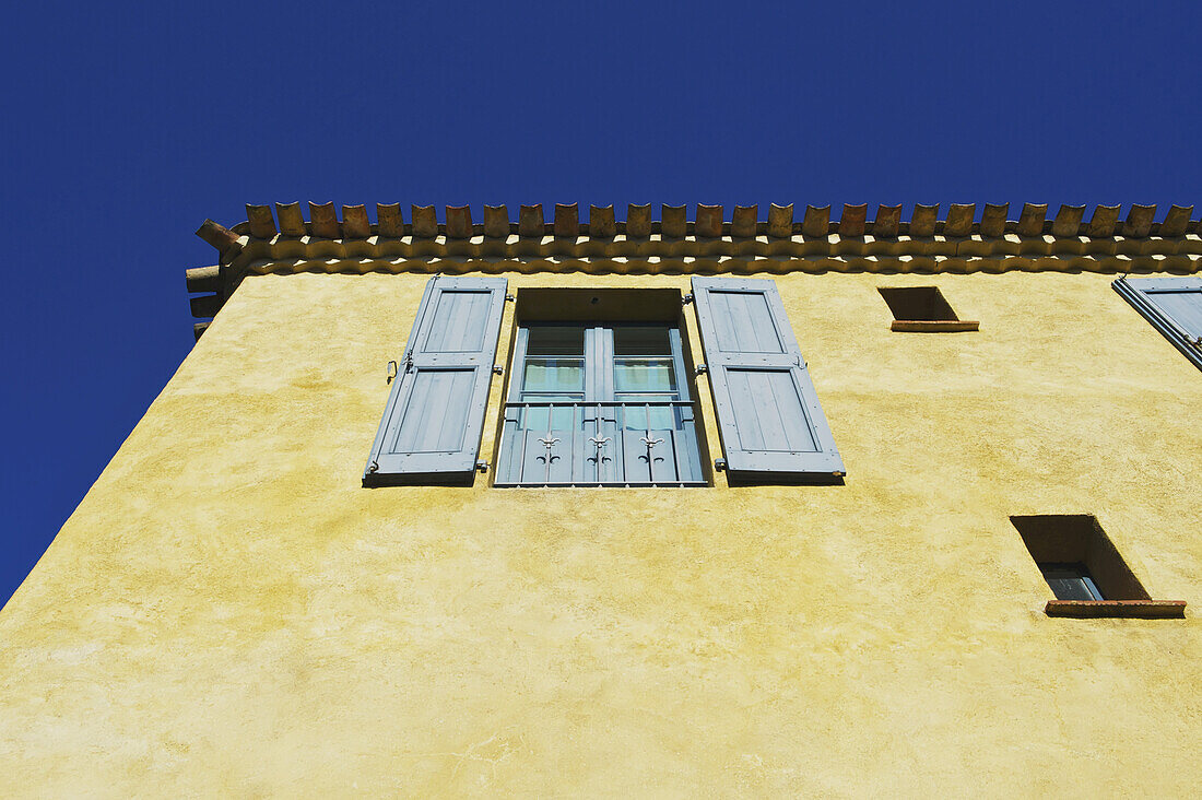 Low Angle View Of A Yellow Building With Blue Shutters On The Windows, Decorative Roofline And A Blue Sky; Cite, France