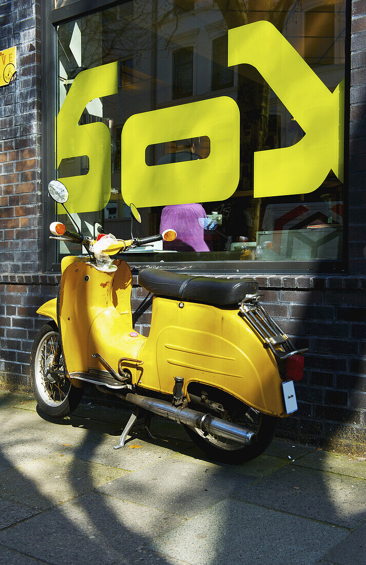 A Yellow Motorcycle Parked Outside A Building With A Large Window And Decal Sign; Hamburg, Germany