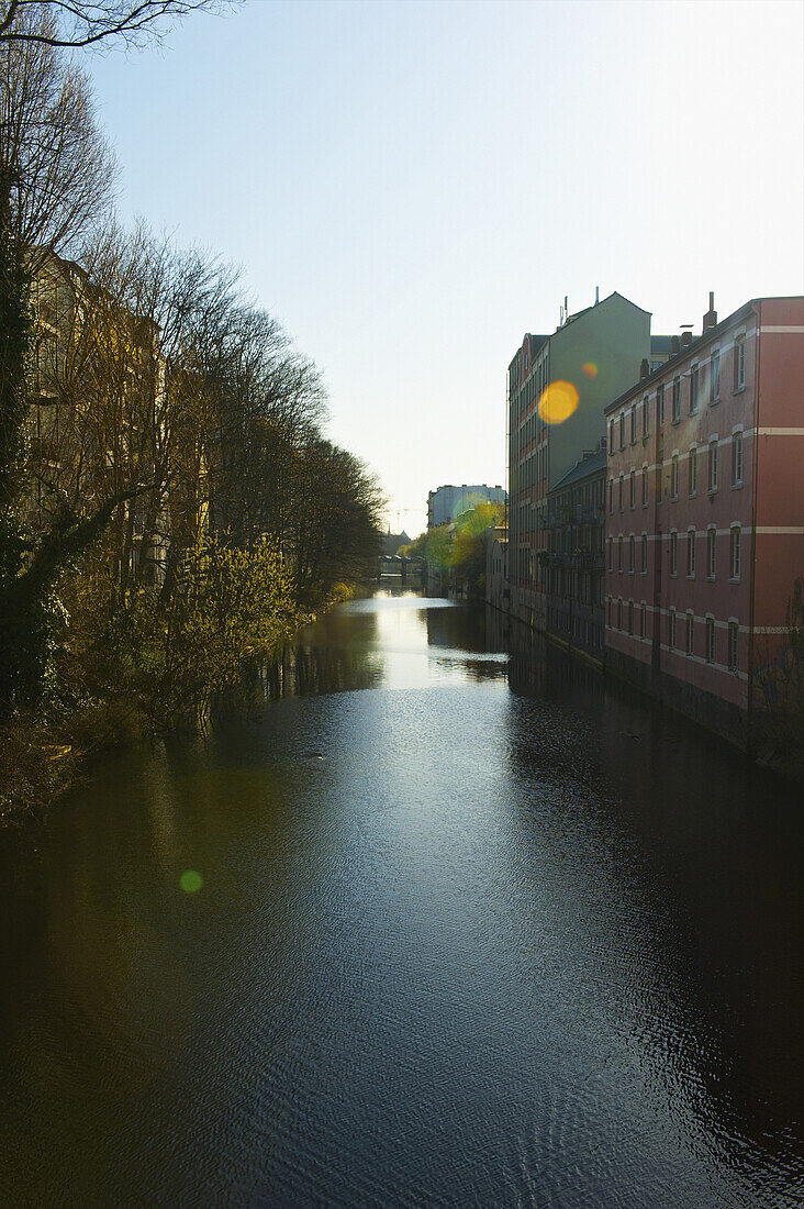 Ein von Bäumen gesäumter Fluss auf der einen und Gebäuden auf der anderen Seite; Hamburg, Deutschland.