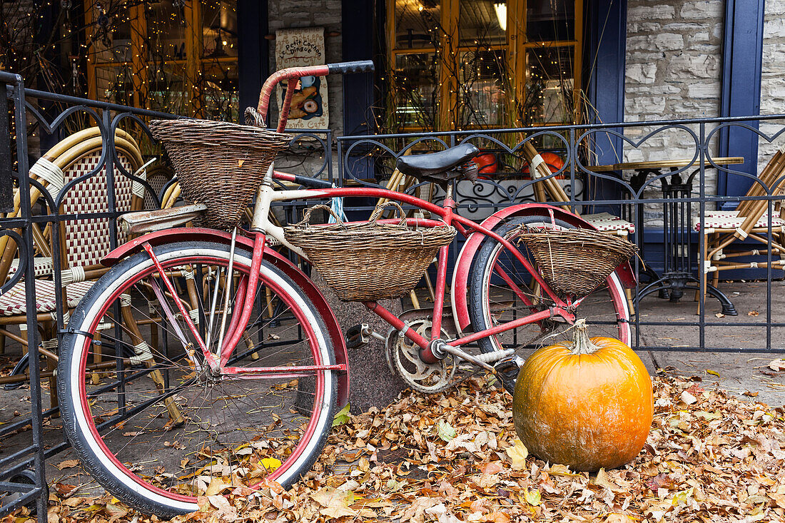 Fahrrad mit Korb, geparkt vor einer Restaurantterrasse mit einem Kürbis und gefallenen Herbstblättern auf dem Boden; Quebec City, Quebec, Kanada