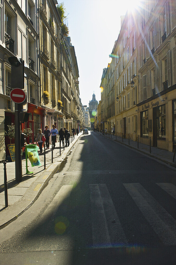 Sonnenlicht scheint auf einen Gehweg mit Fußgängern, Marais-Viertel; Paris, Frankreich