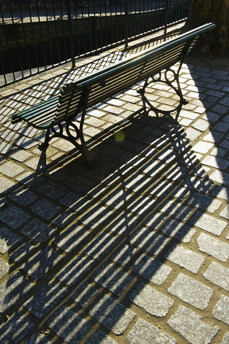 Eine Bank und ein Geländer mit Schattenwurf auf einem Gehweg; Paris, Frankreich