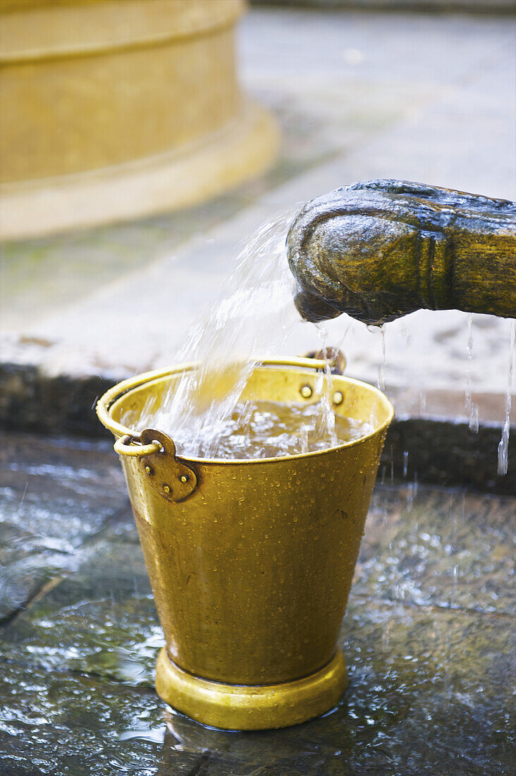 Wasser, das aus einem Wasserhahn in einen kleinen gelben Eimer fließt; Ulpotha, Embogama, Sri Lanka