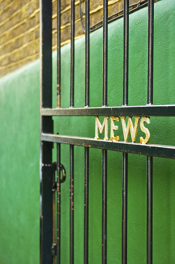 A Metal Gate Open With The Word Mews In Written In Gold Against A Green Wall; London, England