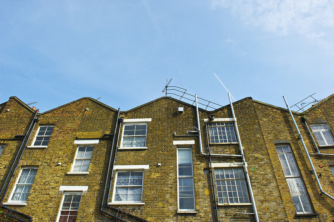 Backstein-Wohngebäude mit Rohren an der Wand und Antenne auf dem Dach; London, England.