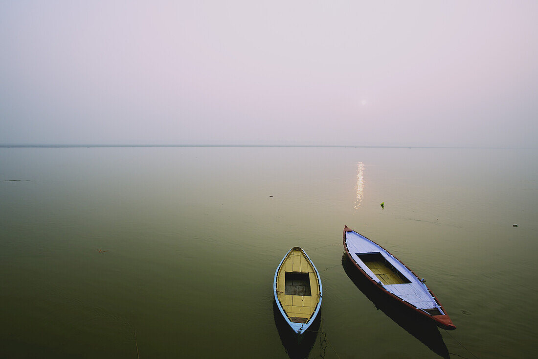 Zwei Holzboote sitzen auf dem ruhigen Wasser des Ganges; Varanasi, Indien