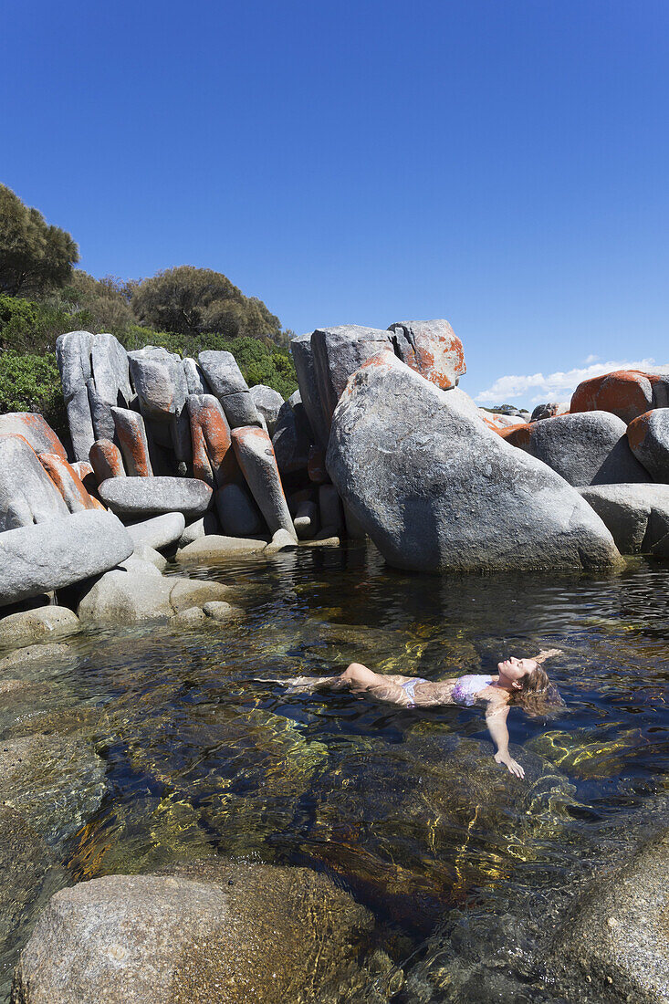 Eine junge Frau schwimmt allein zwischen den großen Felsen am Strand der Bay Of Fires; Tasmanien, Australien