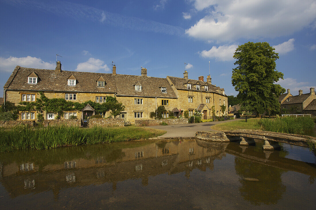 Ein Wohnhaus und seine Spiegelung im Wasser, Lower Slaughter Village, Cotswolds; Gloucestershire, England.