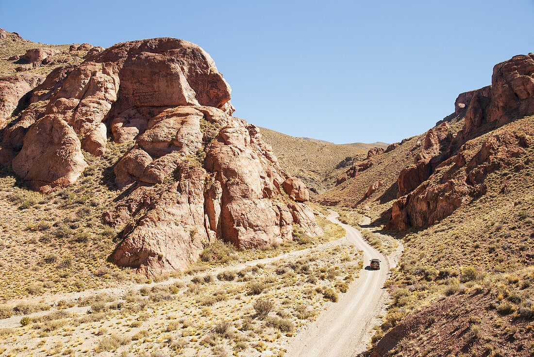 A Car Traveling On A Dirt Road In The Desert And Entering A Canyon; Mendoza, Argentina