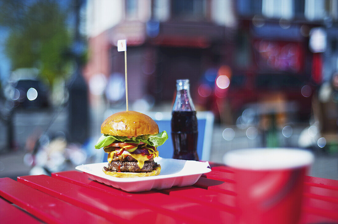 Ein großer Hamburger und eine Flasche Pop auf einem Tisch; London, England.