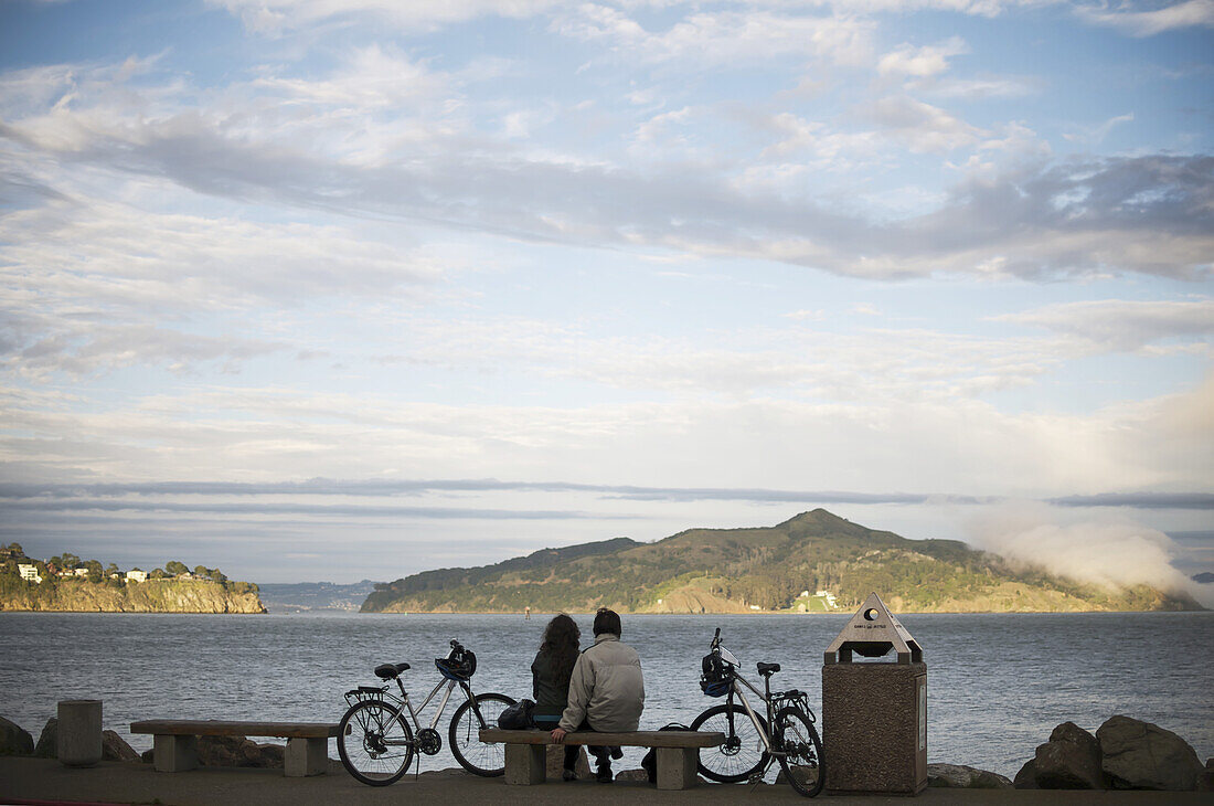 A Couple Sits By San Francisco Bay As The Sun Sets; San Francisco, California, United States Of America