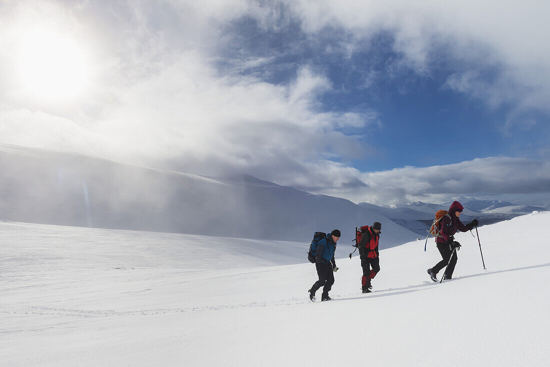 Drei Wanderer auf verschneitem Winterspaziergang beim Aufstieg zum Geal Charn, in der Nähe von Laggan; Schottland.