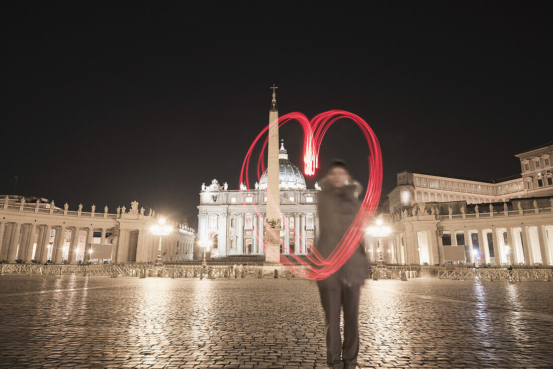 Eine Frau steht mit einer roten Lichterkette in Form eines Herzens auf dem Petersplatz; Rom, Latium, Italien