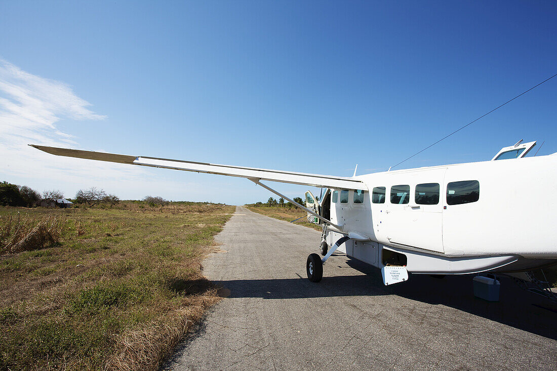 Ein weißes Flugzeug sitzt auf einer Landebahn in einem abgelegenen Gebiet; Vamizi Island, Mosambik