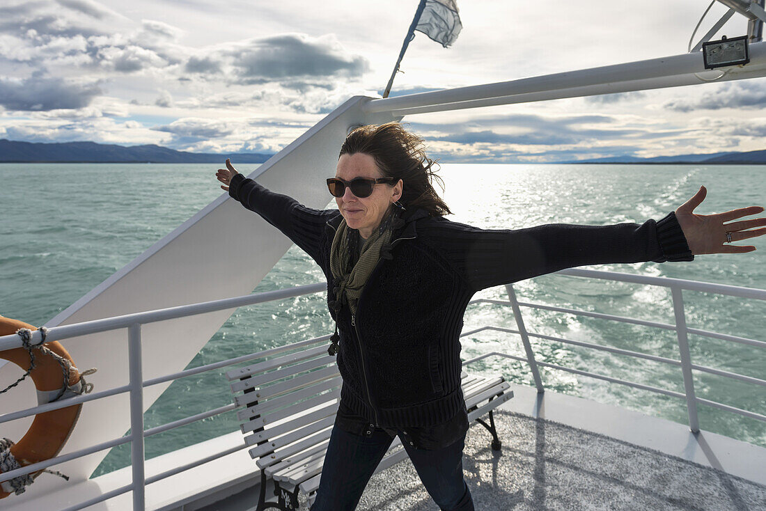 A Woman Standing With Arms Out Against The Wind At The Back Of A Boat On A Lake; Santa Cruz Province, Argentina