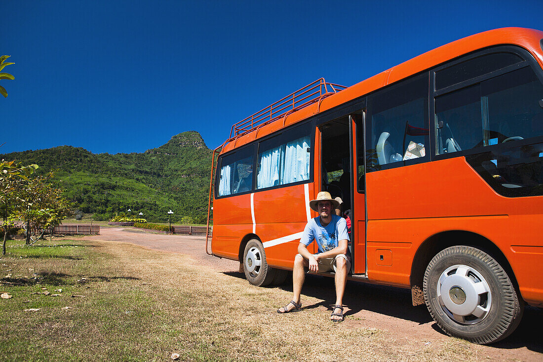 Ein Mann sitzt und wartet in einem Reisebus nach einer Tempeltour; Wat Phu, Laos