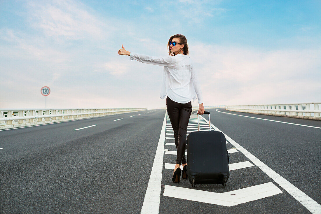 Woman Hitchhiking On A Highway With Her Luggage; Xiamen, Fujian, China