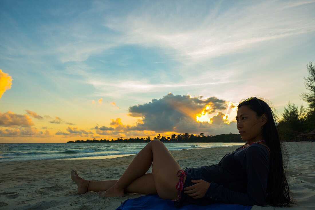 A Young Woman Lays Posing On Sokha Beach At Sunset; Sihanoukville, Cambodia