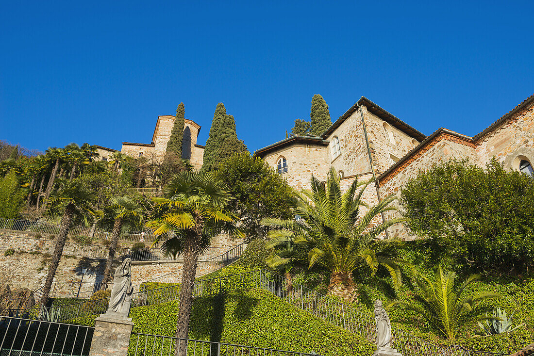 Church Surrounded By Lush Foliage And Palm Trees; Lugano, Ticino, Switzerland