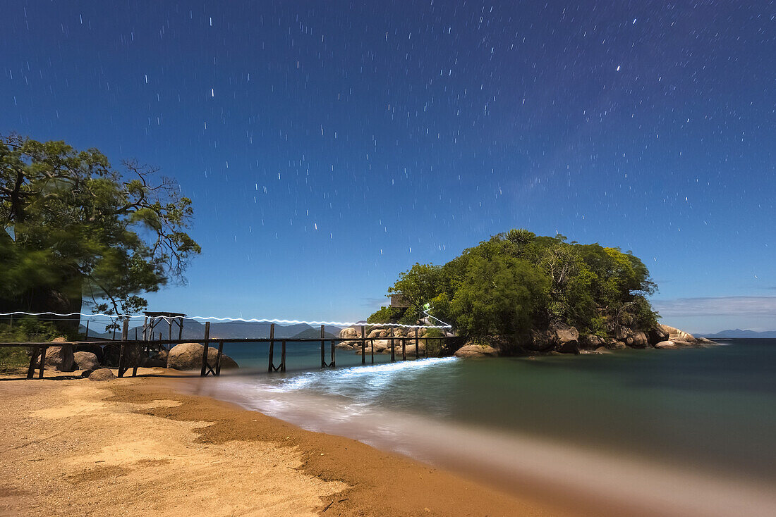 Langzeitbelichtung des Fackelwegs entlang der kleinen Brücke, die von Mumbo Island zu einer kleinen Insel für Touristenunterkünfte führt, unter einem Sternenhimmel, Malawisee; Malawi