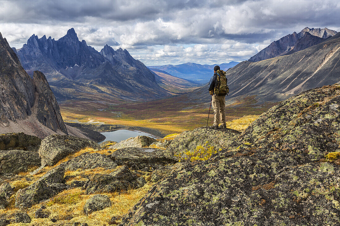 Wanderer steht auf einem Felsen und überblickt die bunten Täler im Tombstone Territorial Park im Herbst; Yukon, Kanada