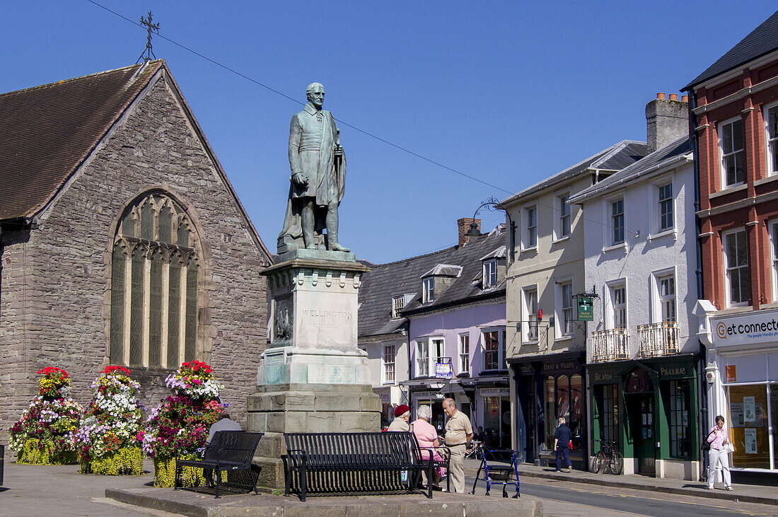 Fußgänger auf malerischer Straße mit Geschäften und einer Kirche; Brecon, Powys, Wales