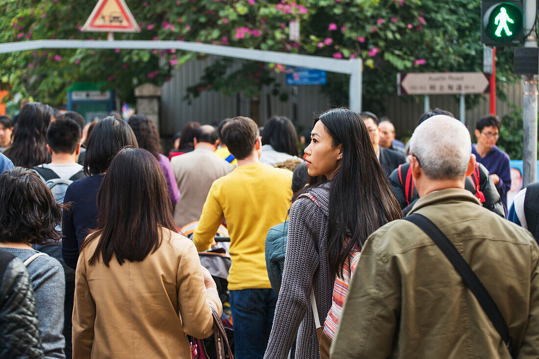 Eine junge Frau mit Rucksack unter vielen Fußgängern auf den belebten Straßen von Kowloon; Hongkong, China