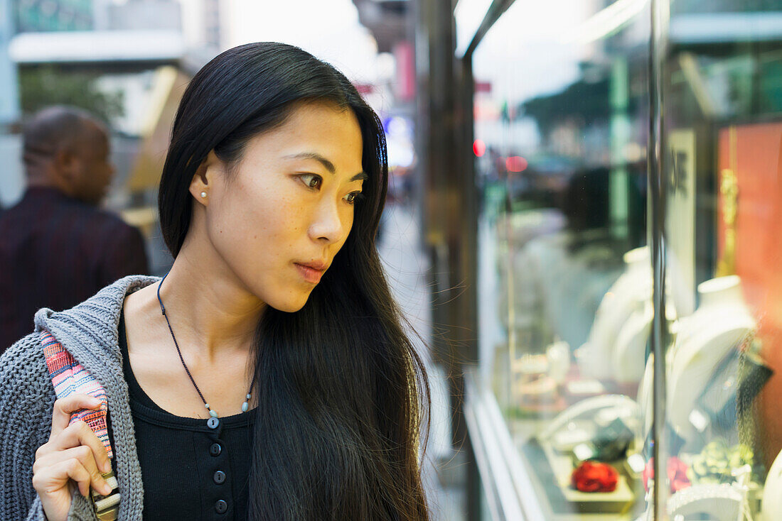 Eine junge Frau beim Schaufensterbummel in den Einzelhandelsgeschäften entlang der Straße, Kowloon; Hongkong, China.