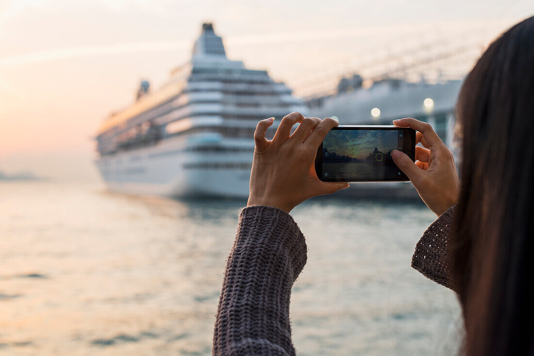 A Young Woman Photographs A Cruise Ship In The Harbour At Sunset, Kowloon; Hong Kong, China