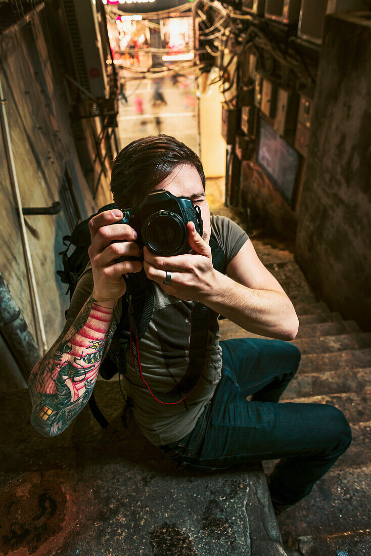 A Male Traveler Taking A Photograph With His Camera In A Narrow Street; Xiamen, Fujian, China