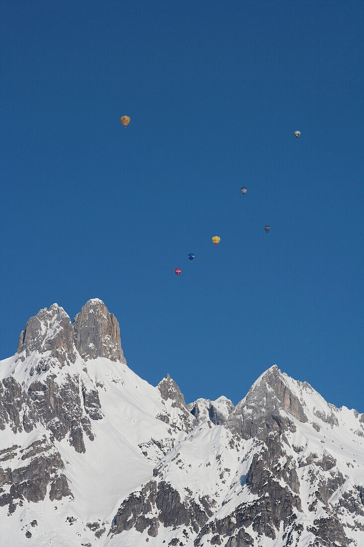 Heißluftballons schweben hoch über den verschneiten Gipfeln der Bischofsmütze während des jährlichen Heißluftballonfestivals des Skigebiets; Filzmoos, Österreich.