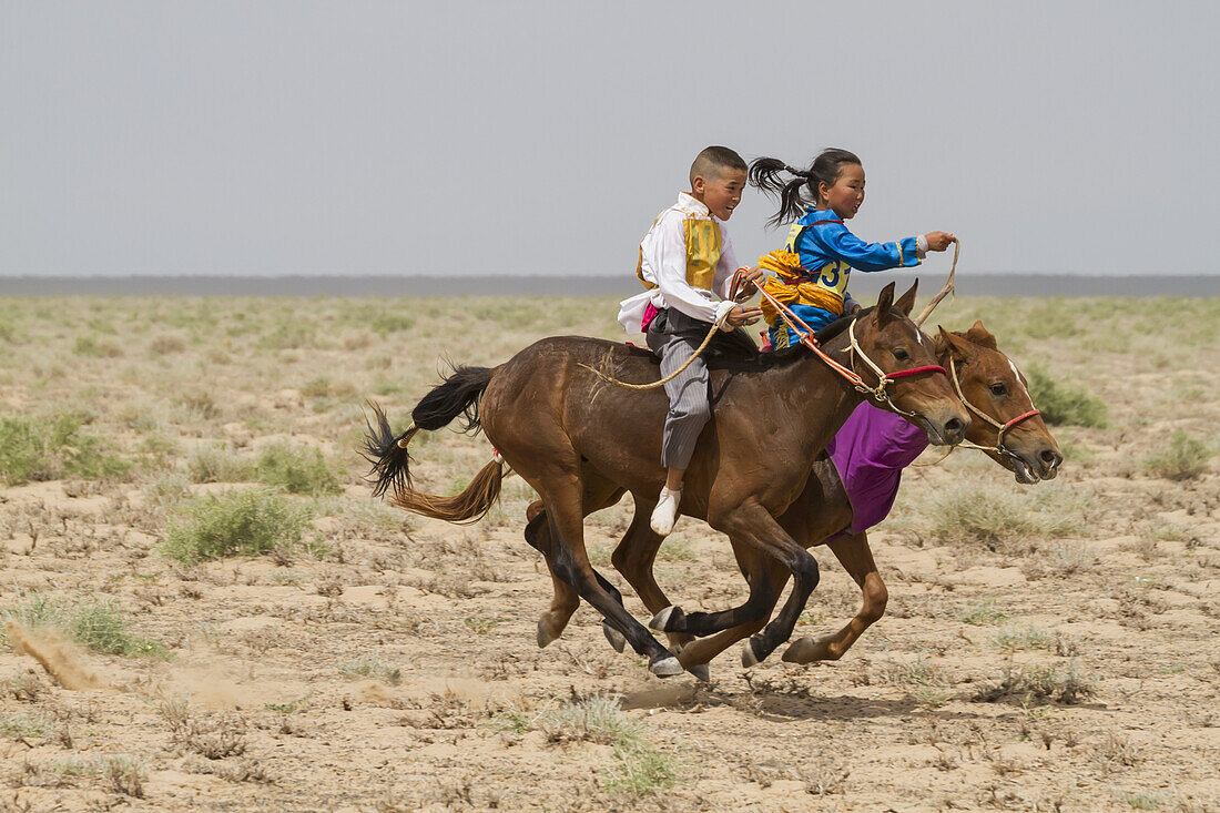 Junge und Mädchen reiten auf Pferden beim Daaga-Pferderennen (Zweijährige) während des Naadam-Festivals in Mandal Ovoo, vEmnv?govi-Provinz, Mongolei