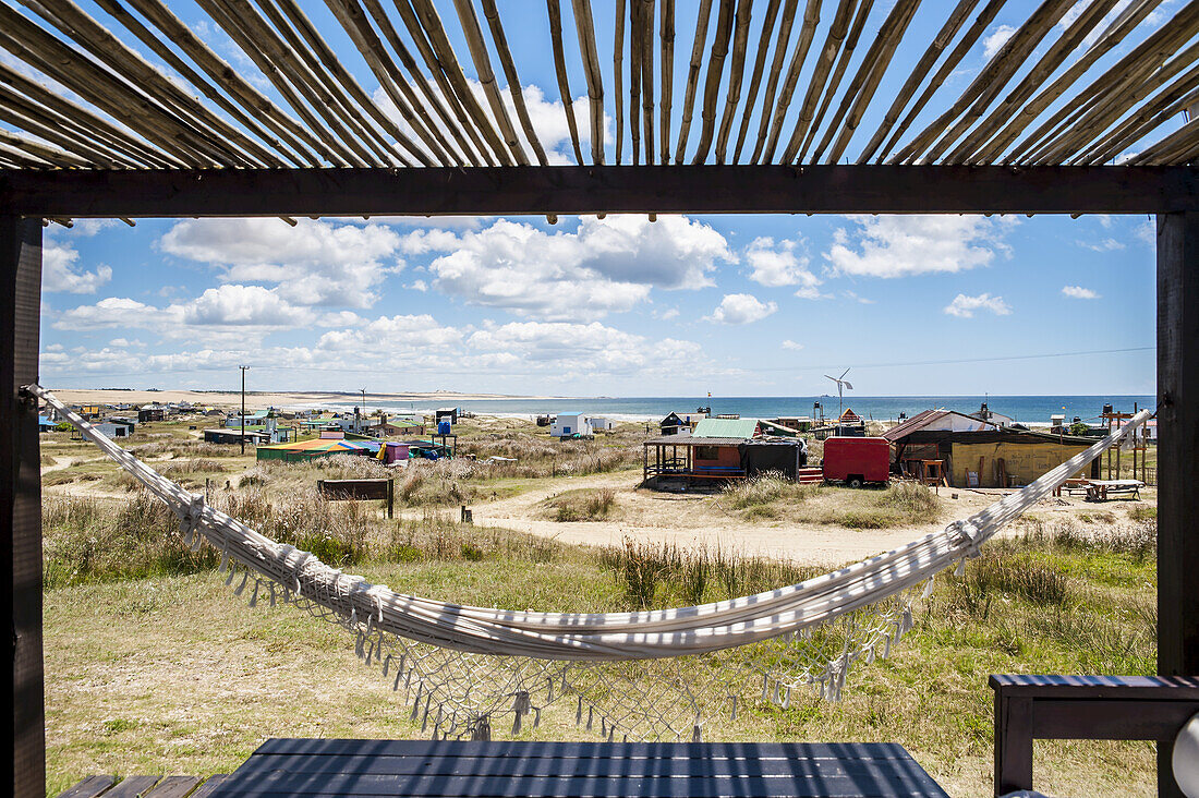 A Hammock Hangs Under A Shaded Porch With Buildings Along The Coast; Cabo Polonio, Uruguay
