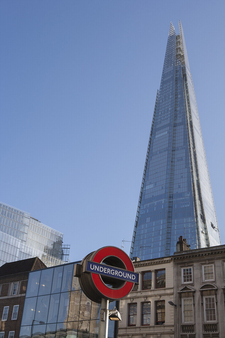 A Sign For The London Underground At London Bridge Station With The Shard By Renzo Piano Rising Above Historical Buildings On Borough High Street; London, England