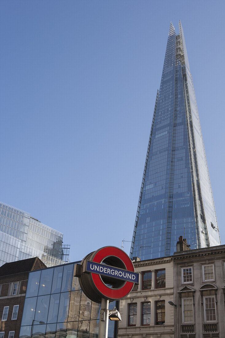 Ein Schild für die Londoner U-Bahn an der Station London Bridge mit dem Shard von Renzo Piano, das sich über historische Gebäude in der Borough High Street erhebt; London, England.