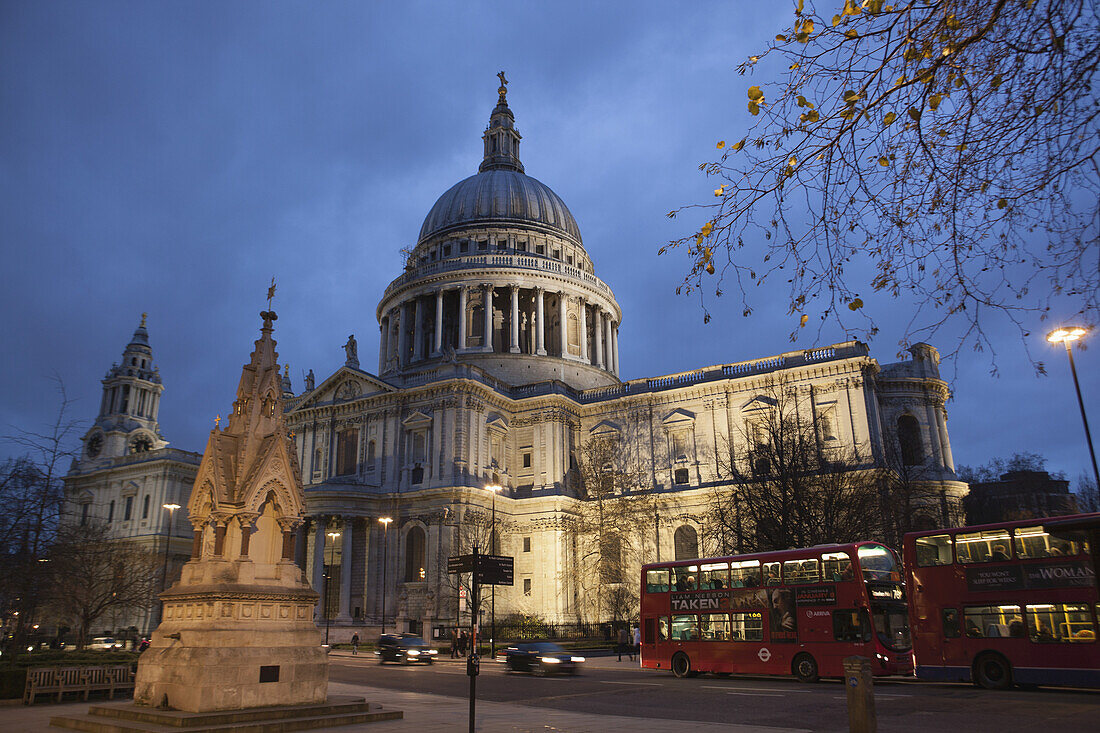 Ein roter London Route Master Doppeldeckerbus fährt in der Abenddämmerung an der St. Paul's Cathedral vorbei, mit dem St. Lawrence Jewry Memorial Fountain im Vordergrund; London, England.