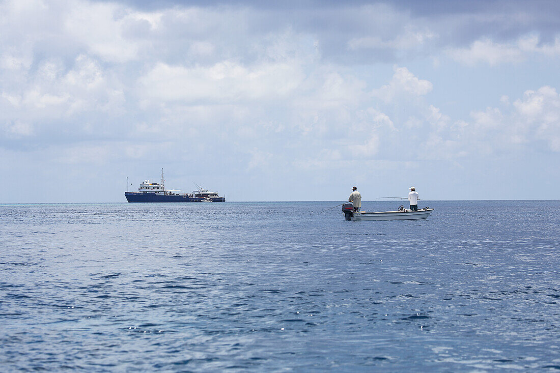 Großes Sportfischerboot in der Ferne und Fischer, die von einem kleineren Boot aus fischen; Tahiti