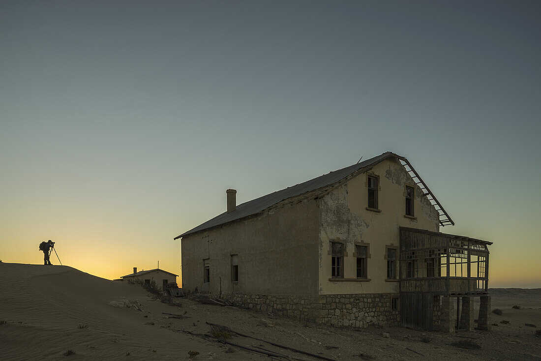 Eine Person macht Fotos von den verlassenen Häusern in der Namib-Wüste bei Sonnenuntergang; Kolmanskop, Namibia