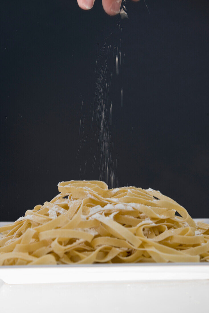 Close up of a hand adding some flour to freshly made tagliatelle pasta