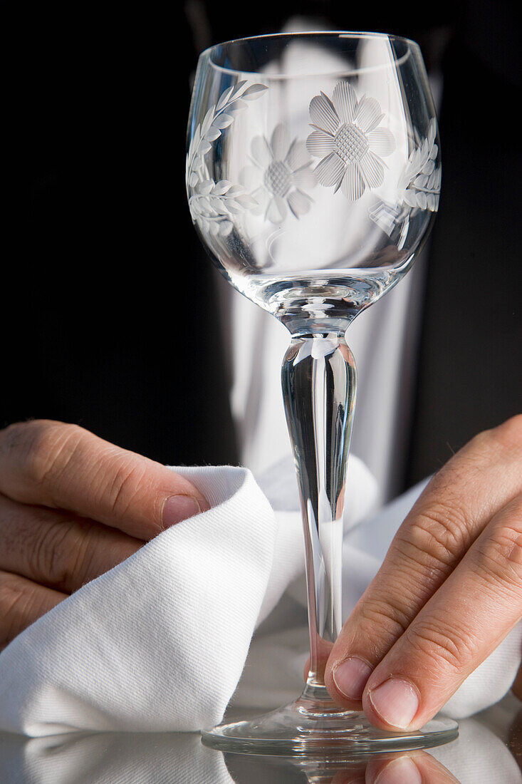 Nahaufnahme eines Kellners, der mit seinen Händen ein Kristallglas poliert