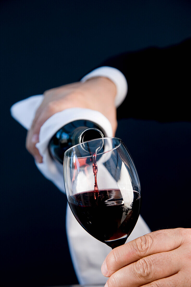 Nahaufnahme eines Kellners, der eine Flasche in der Hand hält und Rotwein in ein Glas gießt